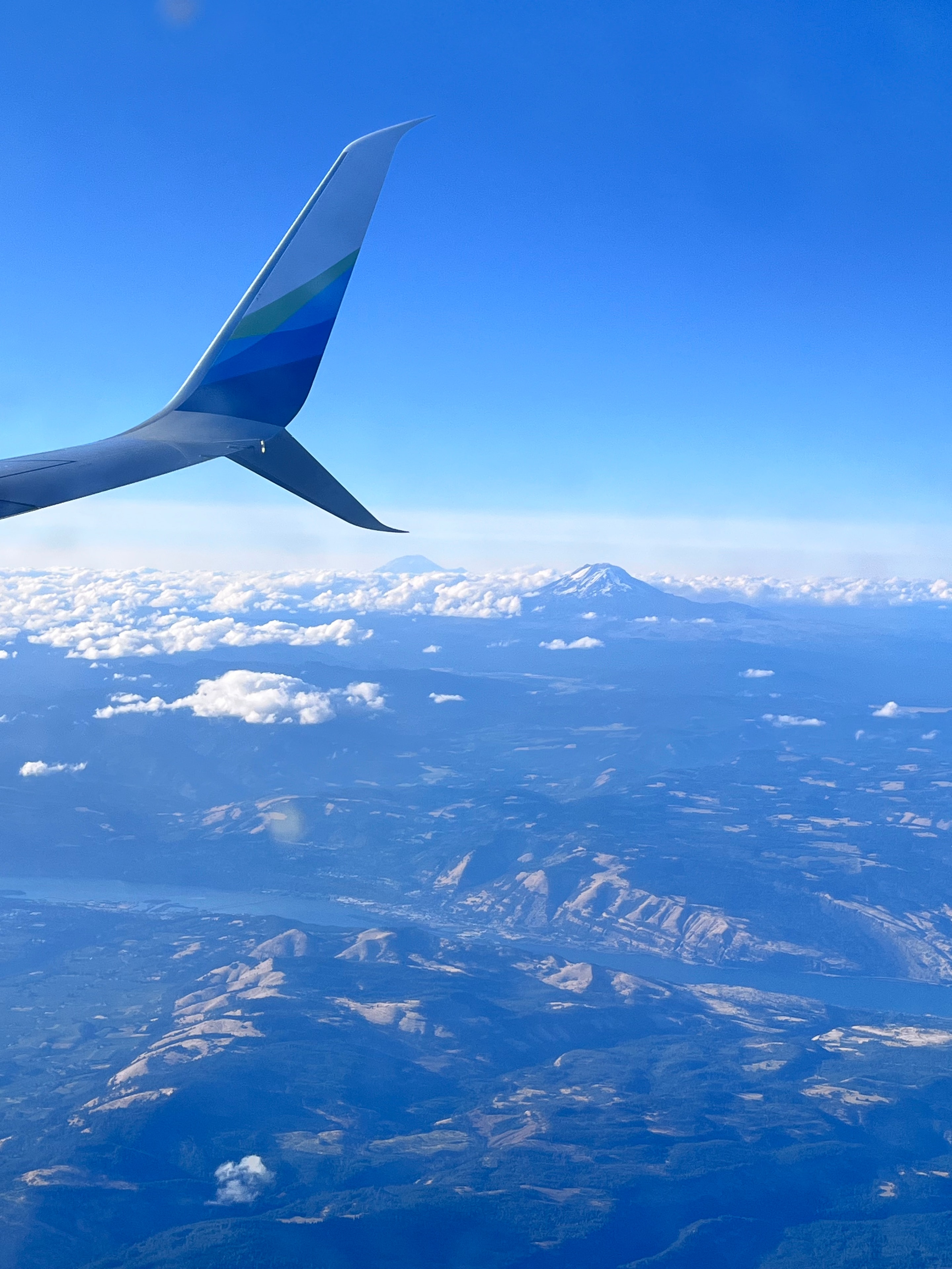 Airplane tail fin against vivid blue sky with mountain range below